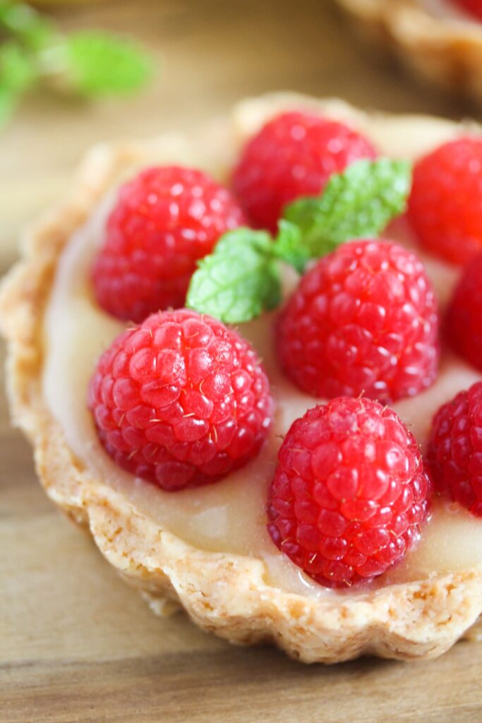 one tart with lemon filling and jewel like raspberries on top