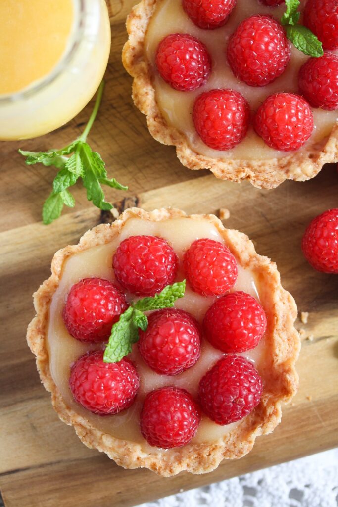 two lemon curd raspberry tarts on a wooden board