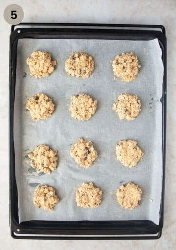 unbaked muesli cookies with nuts and dried fruit in heaps on the baking sheet.