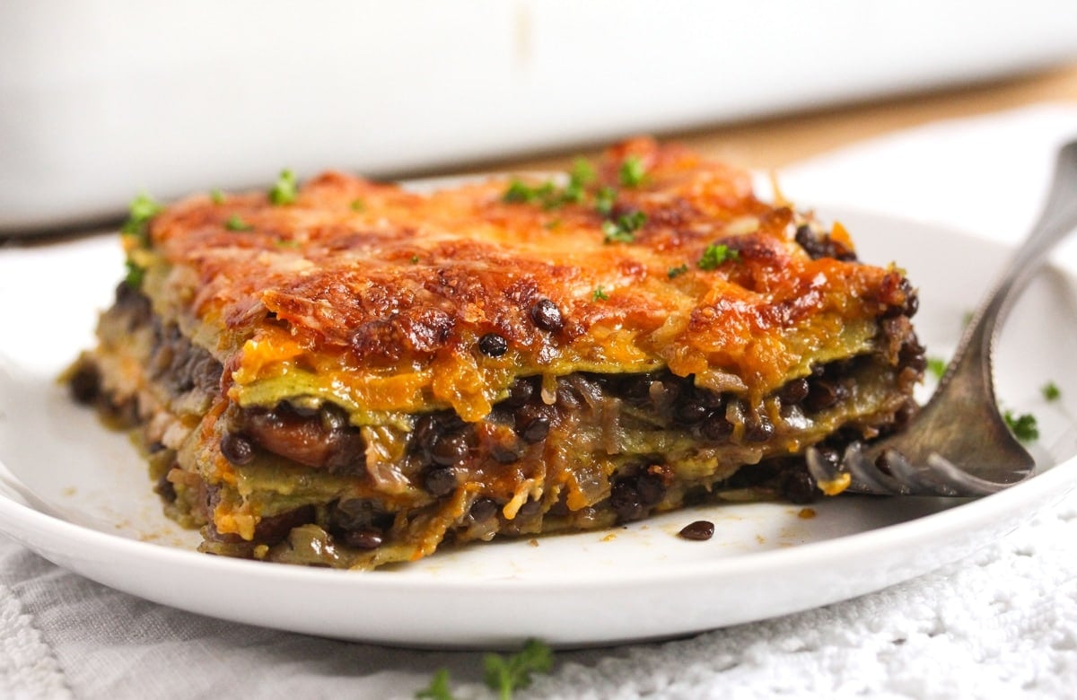 a slice of lasagna with lentils on a small white plate with fork.