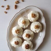 seven carrot cupcakes topped with frosting and walnuts on a vintage platter.