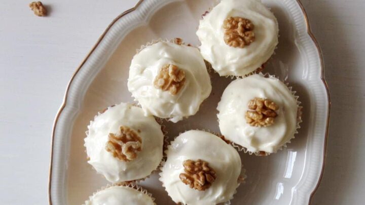 seven carrot cupcakes topped with frosting and walnuts on a vintage platter.