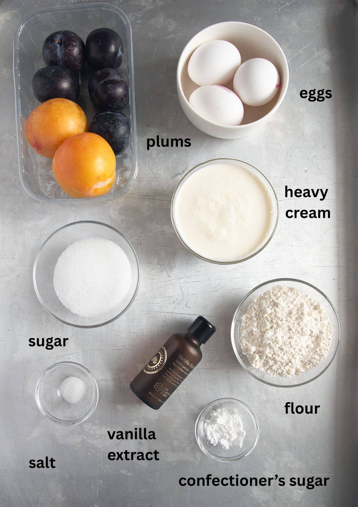 labeled ingredients for making clafoutis with plums, flour, sugar, cream, eggs, and vanilla.