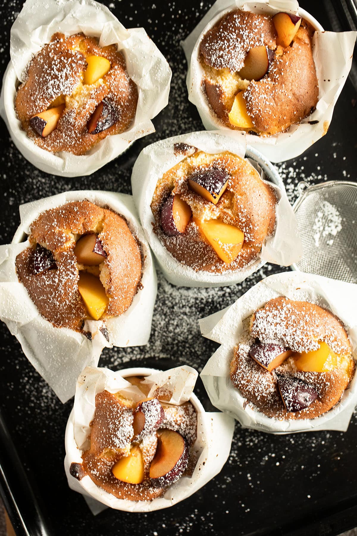 six plum clafoutis in small ramekin dishes lined with white parchment paper.