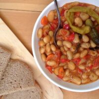 bowl of white bean stew served with bread and gherkins on a kitchen cloth