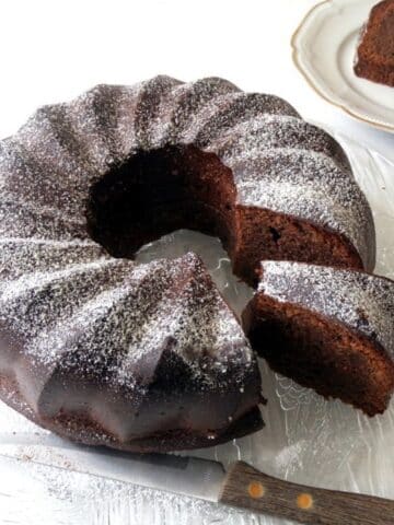 flourless chocolate bundt cake sliced on a vintage platter with a small knife.