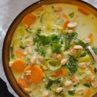 curried african soup with whole peanuts, carrots and leeks in a brown bowl.