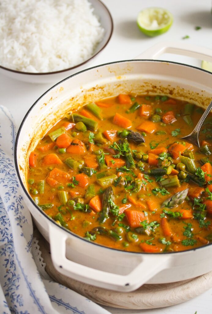 white cast iron pot with indian curry with asparagus and coconut