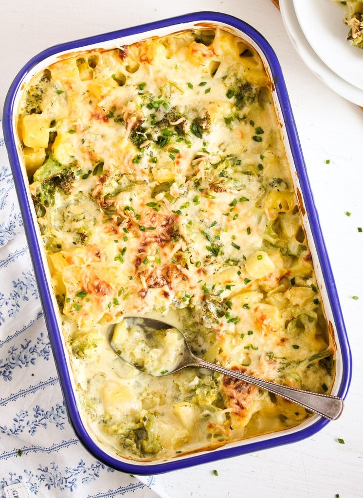 potato broccoli bake in a casserole dish with a spoon in it showing the creamy sauce.