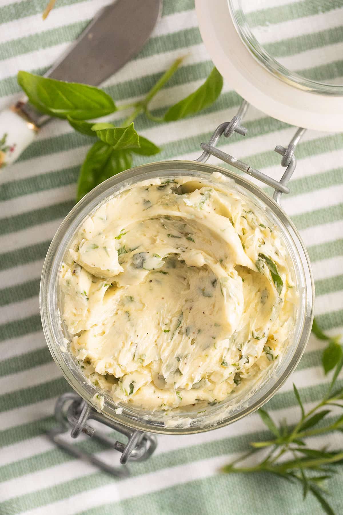 garlic and herb butter in a jar, basil and thyme leaves beside it.