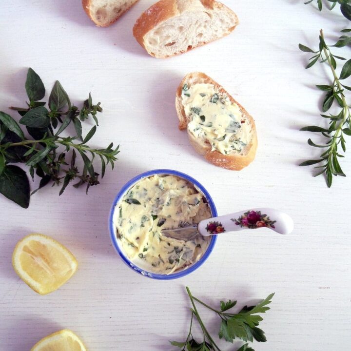 small pot with garlic butter, bread slices, herbs and lemon on the table.