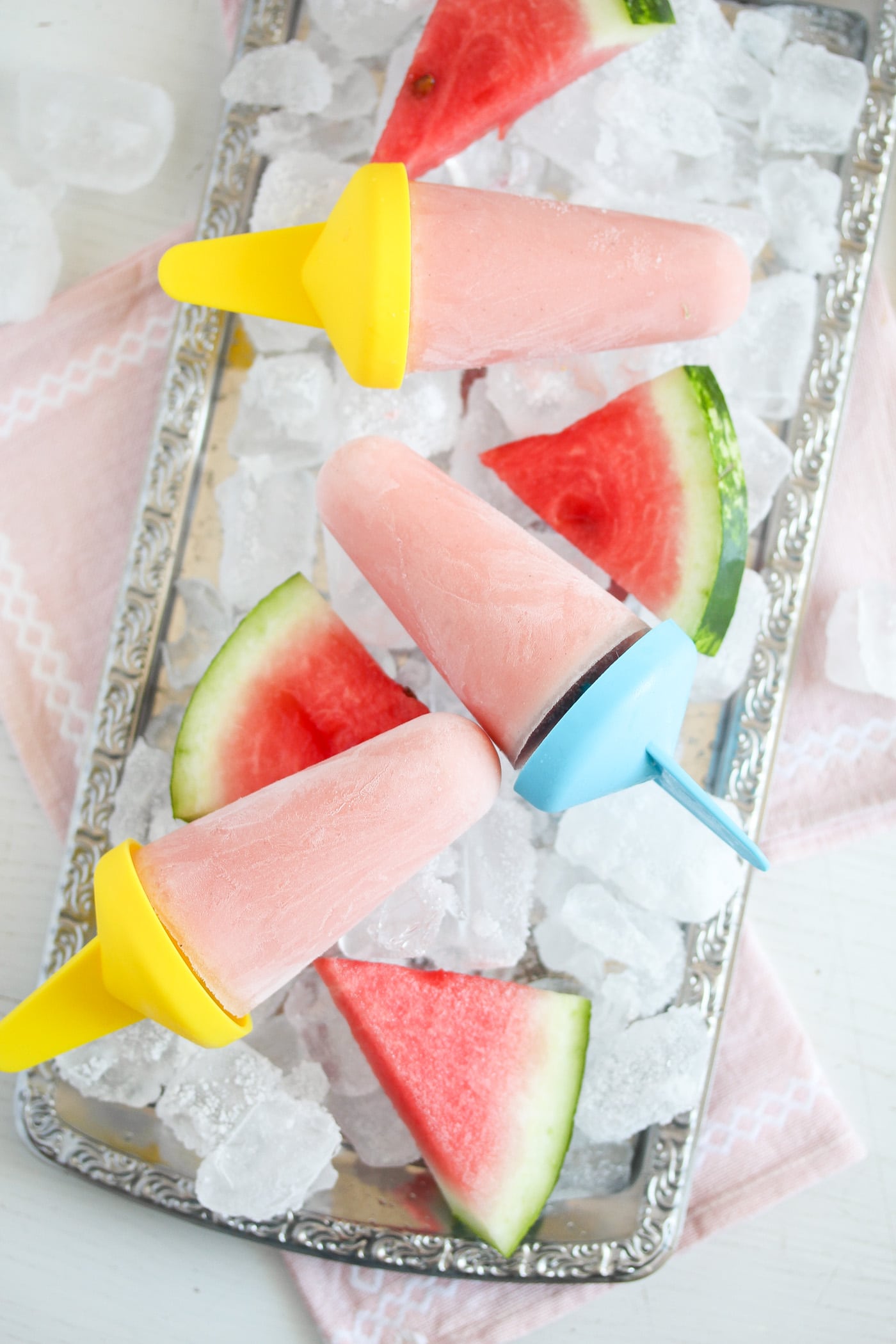 three watermelon ice lollies on a tray with ice cubes