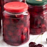 jars of canned cherries and some fresh cherries on the table.