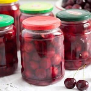 several jars of preserved cherries and two cherries on the table.