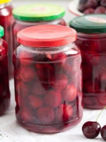 several jars of preserved cherries and two cherries on the table.