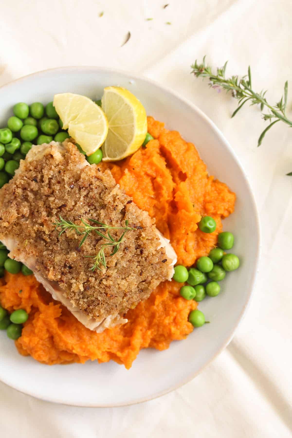 close up of plate with crusted salmon on top of mashed sweet potatoes with peas and limes.