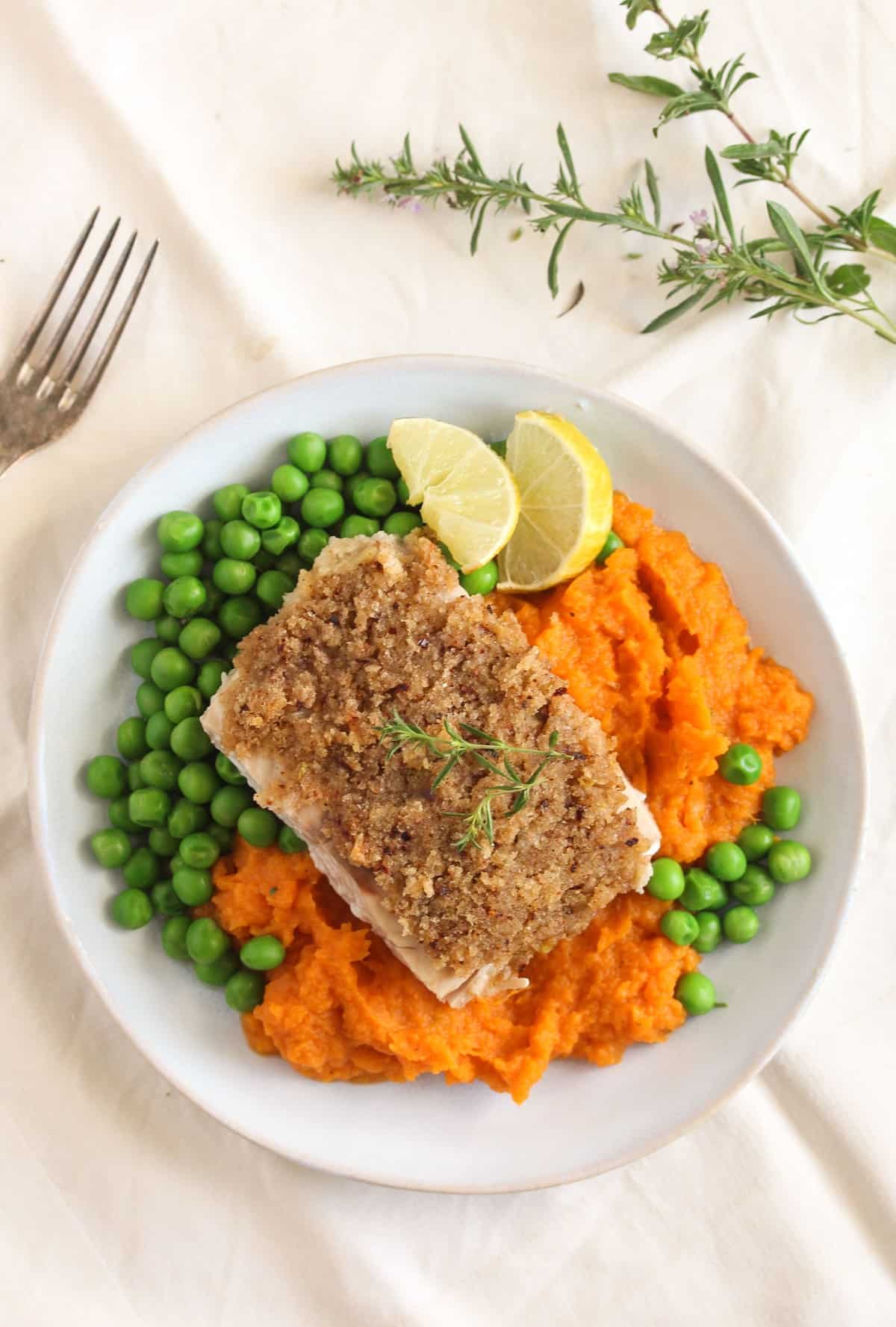 overhead view of a plate of salmon served with mashed sweet ptoatoes and peas.