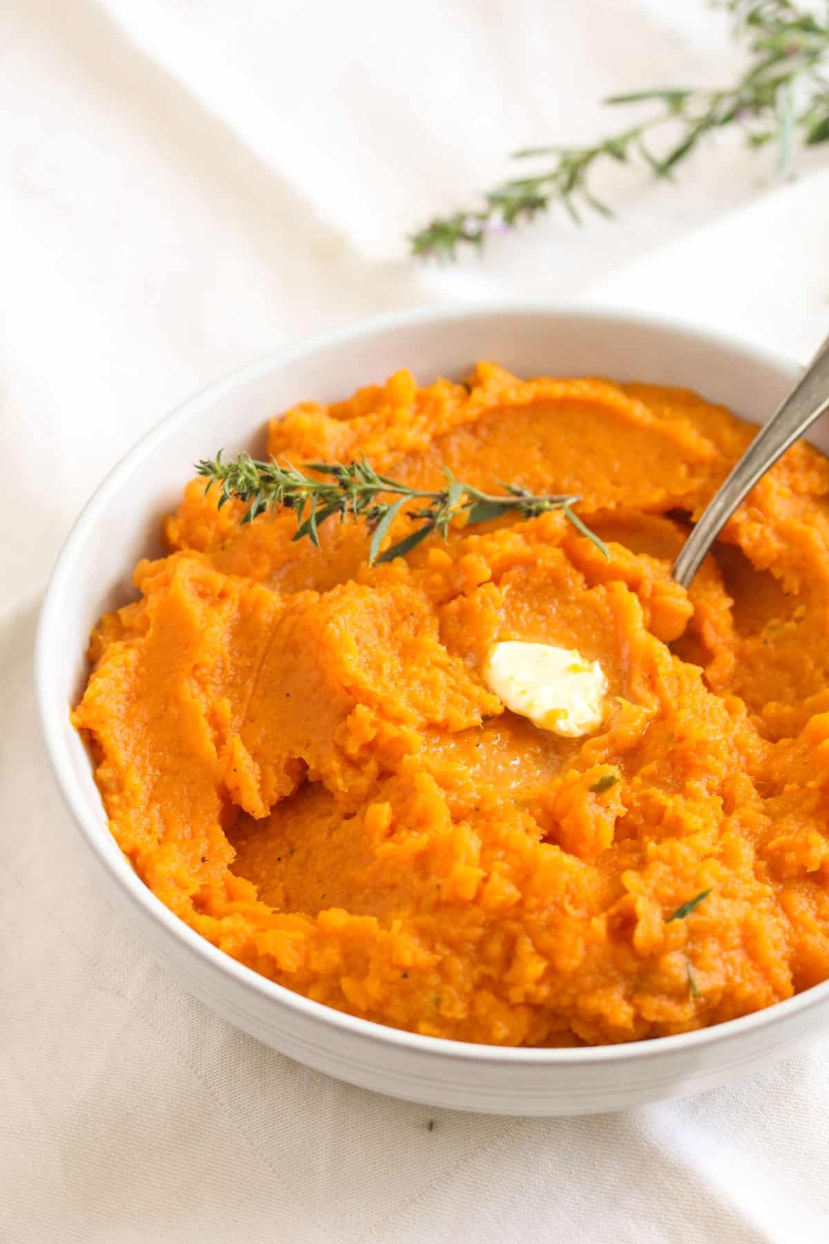 bowl of sweet potato mash topped with butter and fresh tyhme leaves.