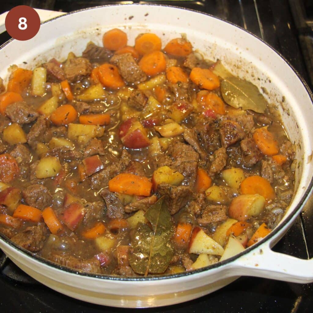 beef stew with apples being cooked in a white dutch oven.