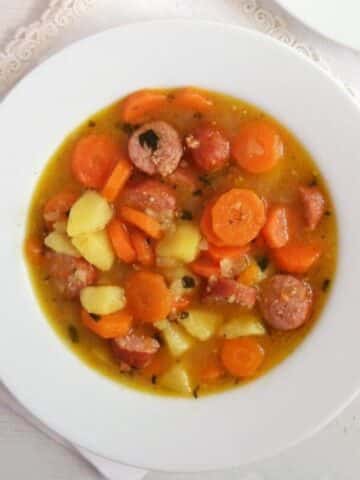 kid-friendly soup with potatoes, carrots and sausage served in a white plate.