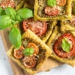 puff pastry canapes with tomatoes and basil piled on a cutting board.
