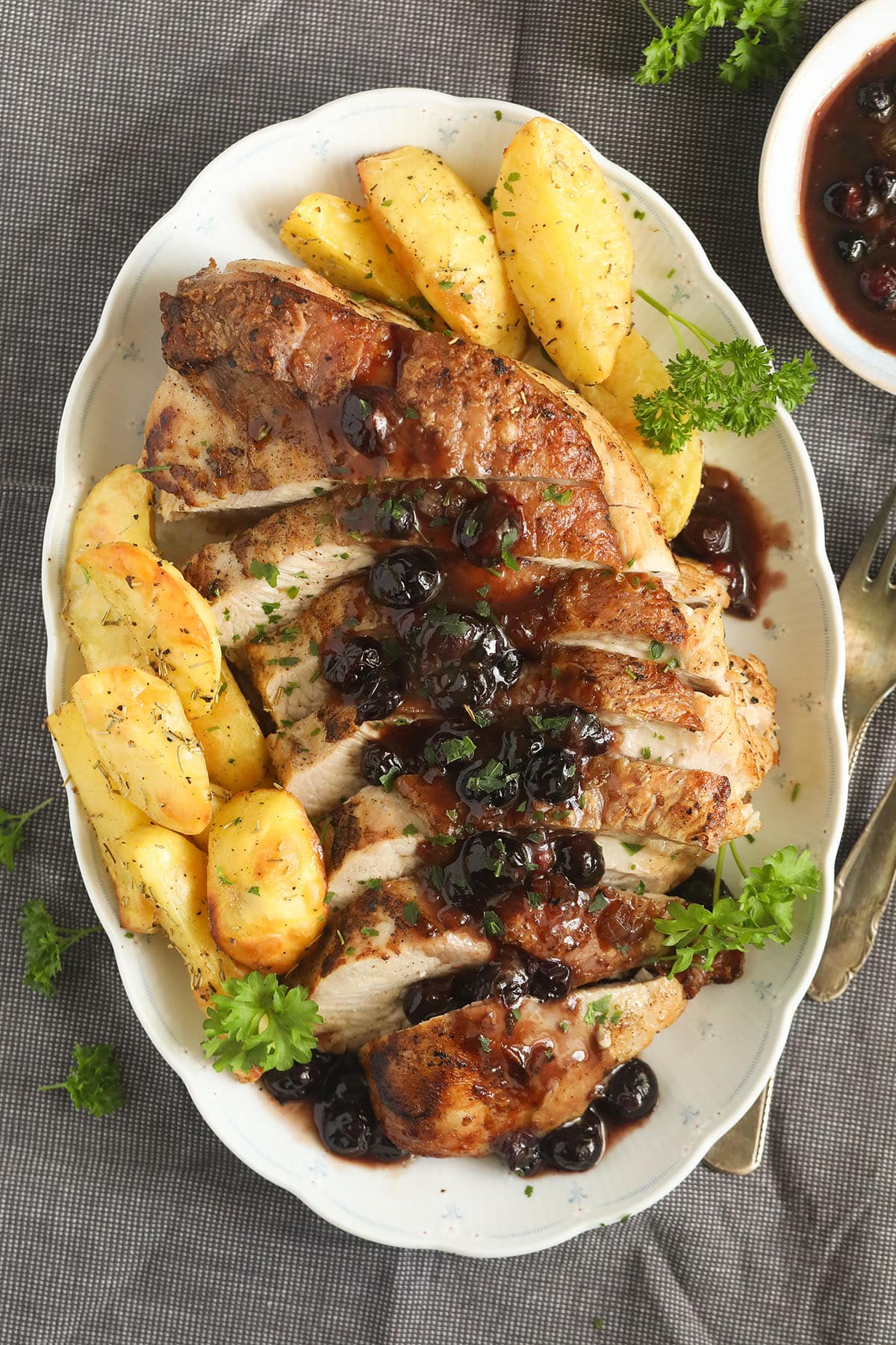 sliced blueberry turkey breast served with roasted potatoes and fresh parsley on a large platter.