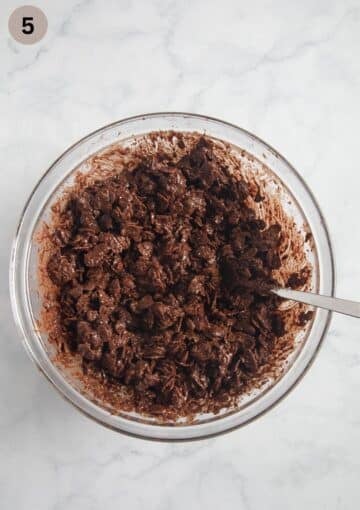 mixing cornflakes into melted chocolate to make chocolate crossiees in a large bowl.