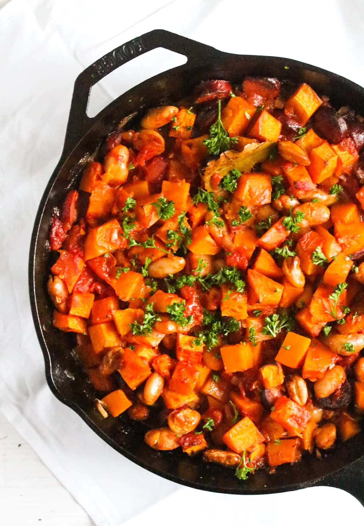 skillet with beans, cabanossi, pumpkin and parsley on top.