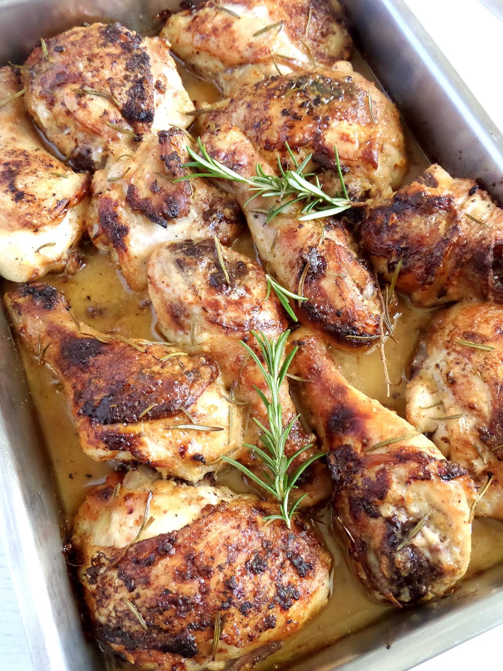 many chicken thighs in a roasting tin with fresh rosemary on top.