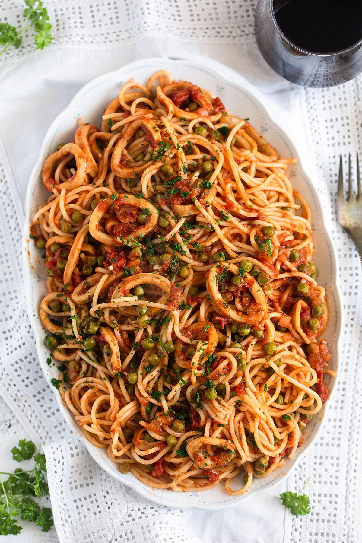 an oval platter with calamari pasta and a glass of red wine.