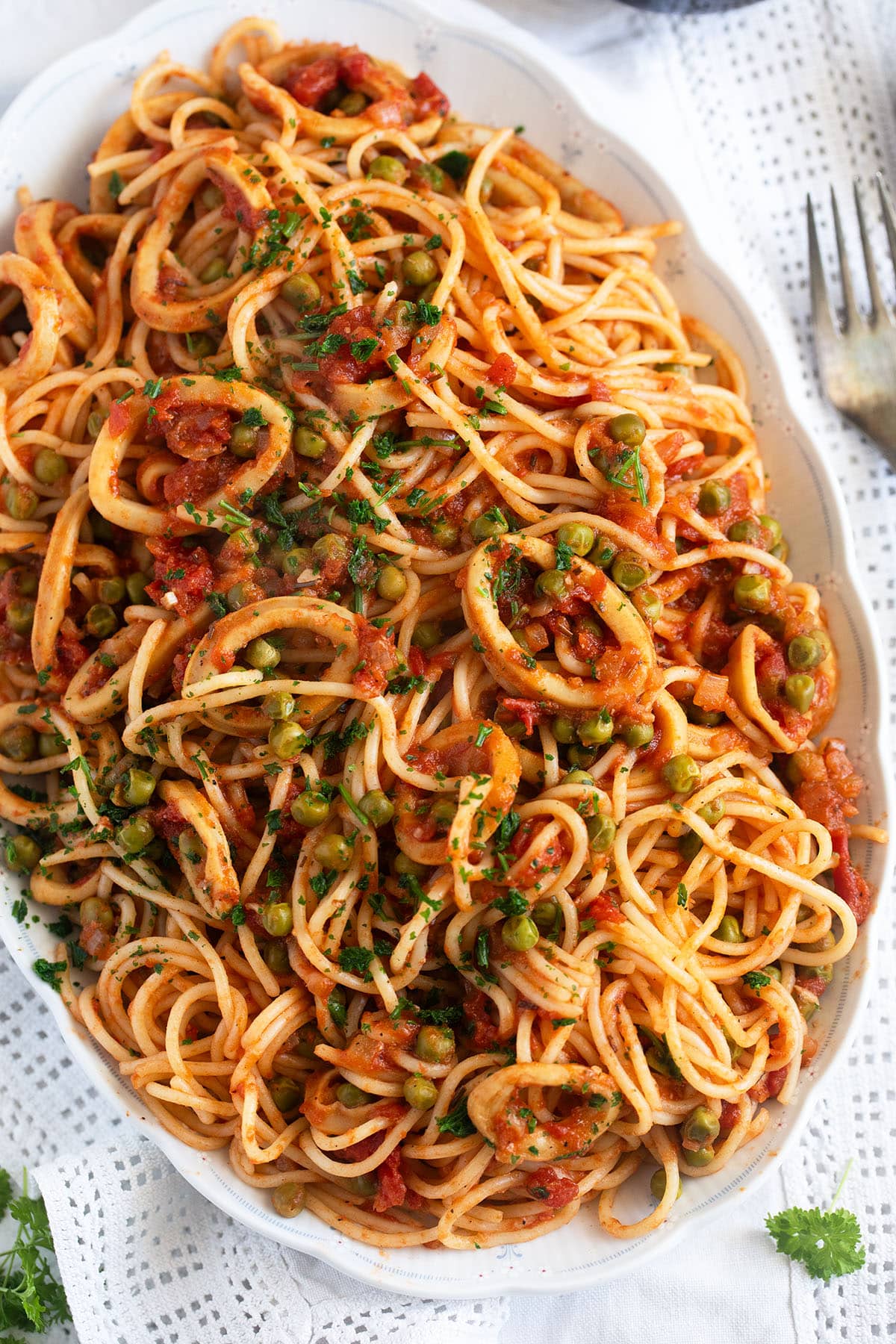 calamari pasta with tomato and pea sauce on a large serving platter, a fork beside it.