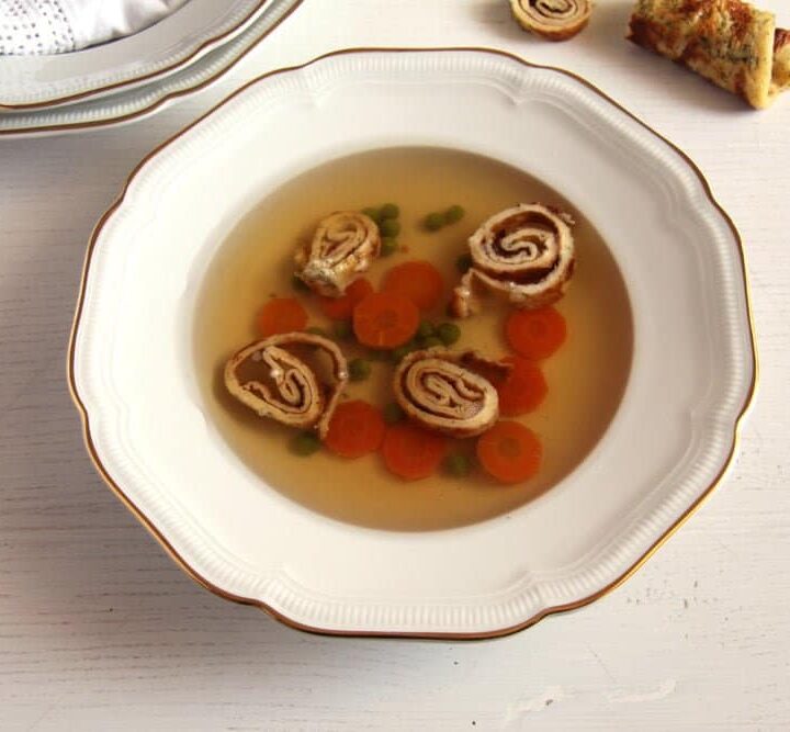 beef broth in a vintage plate served with pancake pieces and carrots.