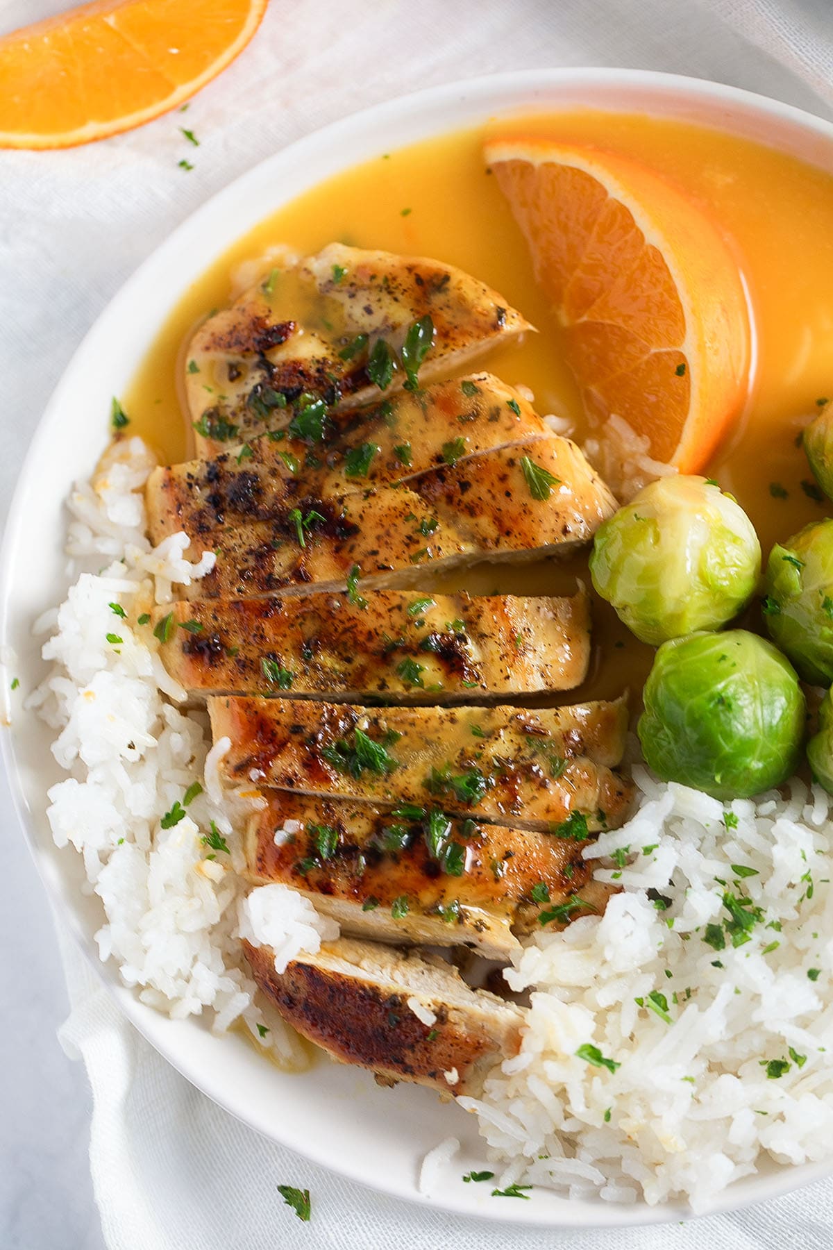 sliced chicken breast served with orange sauce, rice, and brussels sprouts.