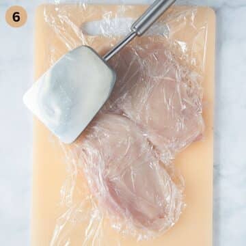 pounding chicken breast between sheets of plastic wrap with a meat mallet.
