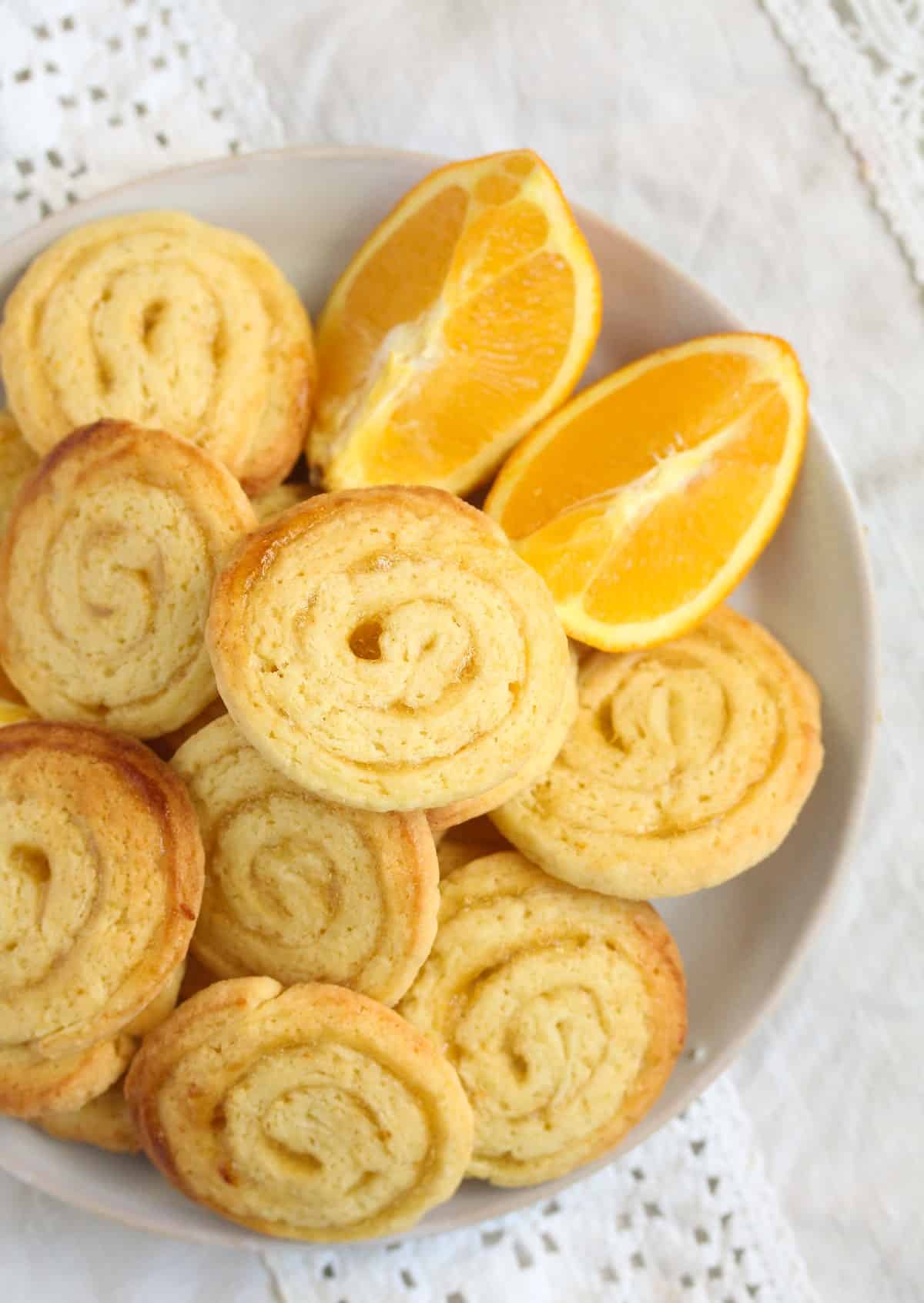 swirl cookies filled with orange jam and two orange wedges on a plate.