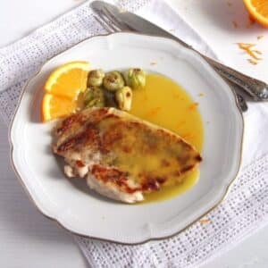 chicken breast with orange sauce, orange slices and brussels sprouts on a vintage plate.