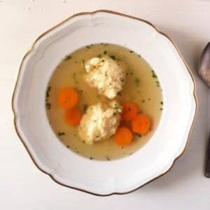 romanian dumpling soup with two dumplings and chopped carrots in a vintage plate.