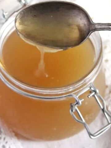 turkey bone broth being poured from a tablespoon in a jar.