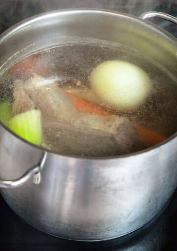 broth, onions, and carrots simmering in a silver soup pot.
