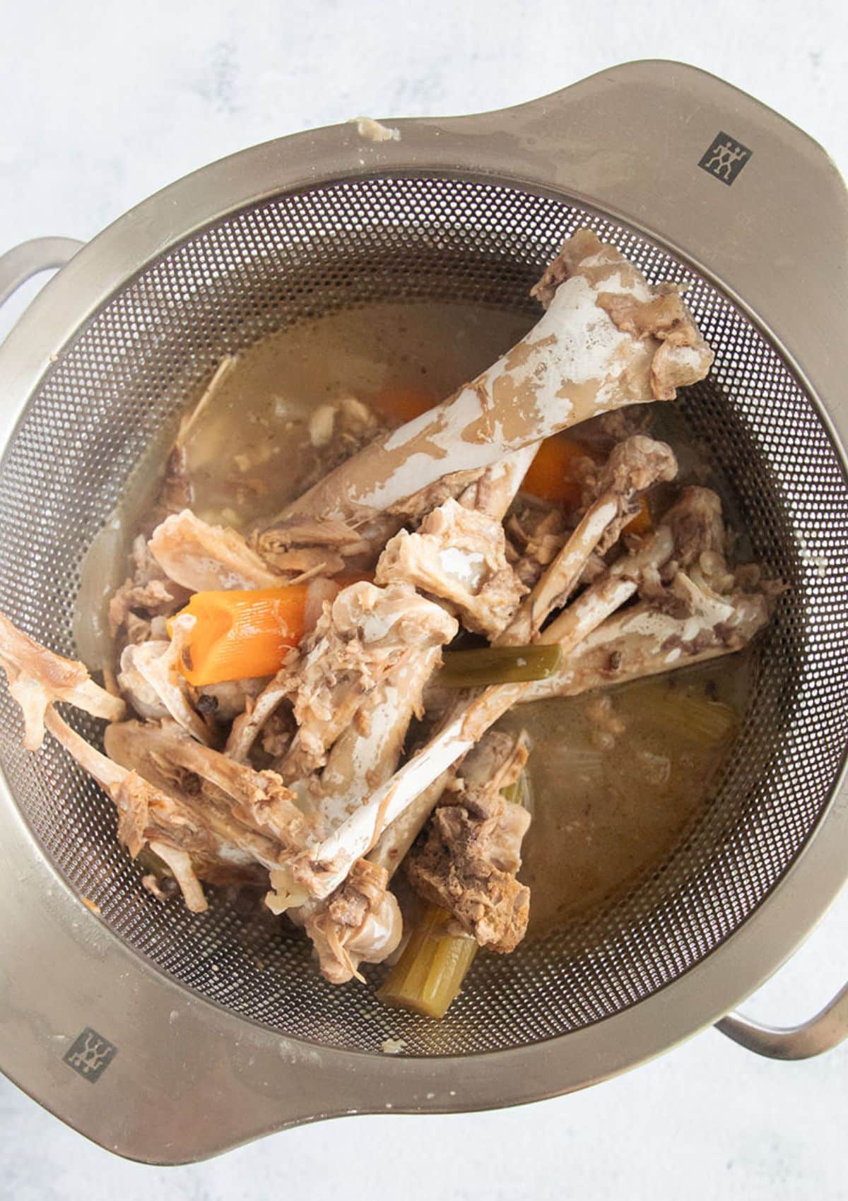 straining broth through a sieve leaving the bones and vegetables behind.