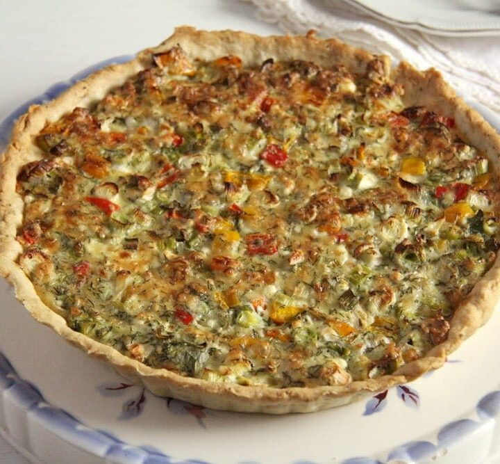 green onion quiche with veggies and cheese on a vintage platter with blue edges.