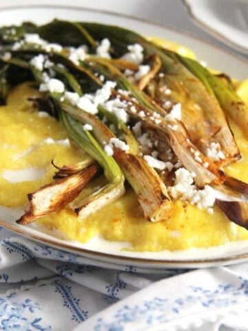 roasted green onions on a platter with polenta and cheese