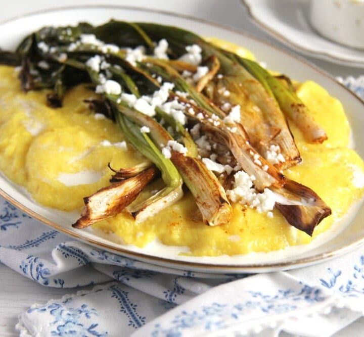 roasted green onions on a platter with polenta and cheese