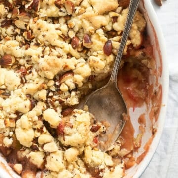 casserole dish filled with crumble with rhubarb and apples with a spoon scooping the dessert.