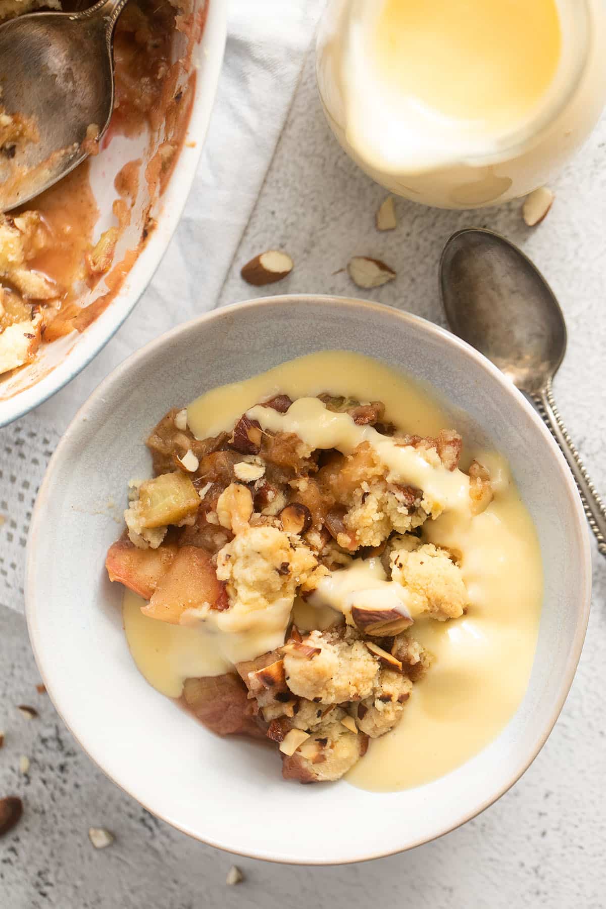 bowl of apple and rhubarb crumble topped with smooth vanilla sauce.