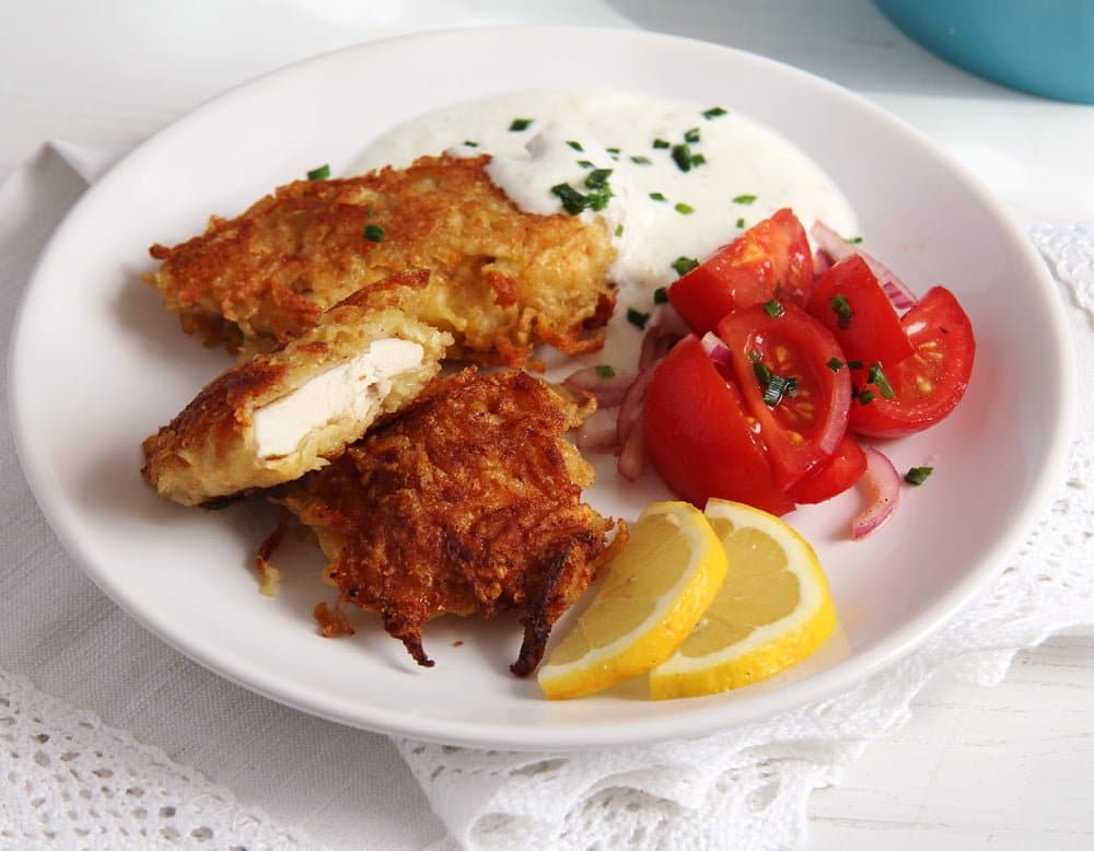 pieces of potato crusted chicken on a plate served with tomatoes and dip