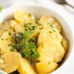 german potato salad sprinkled with chives in a white bowl.