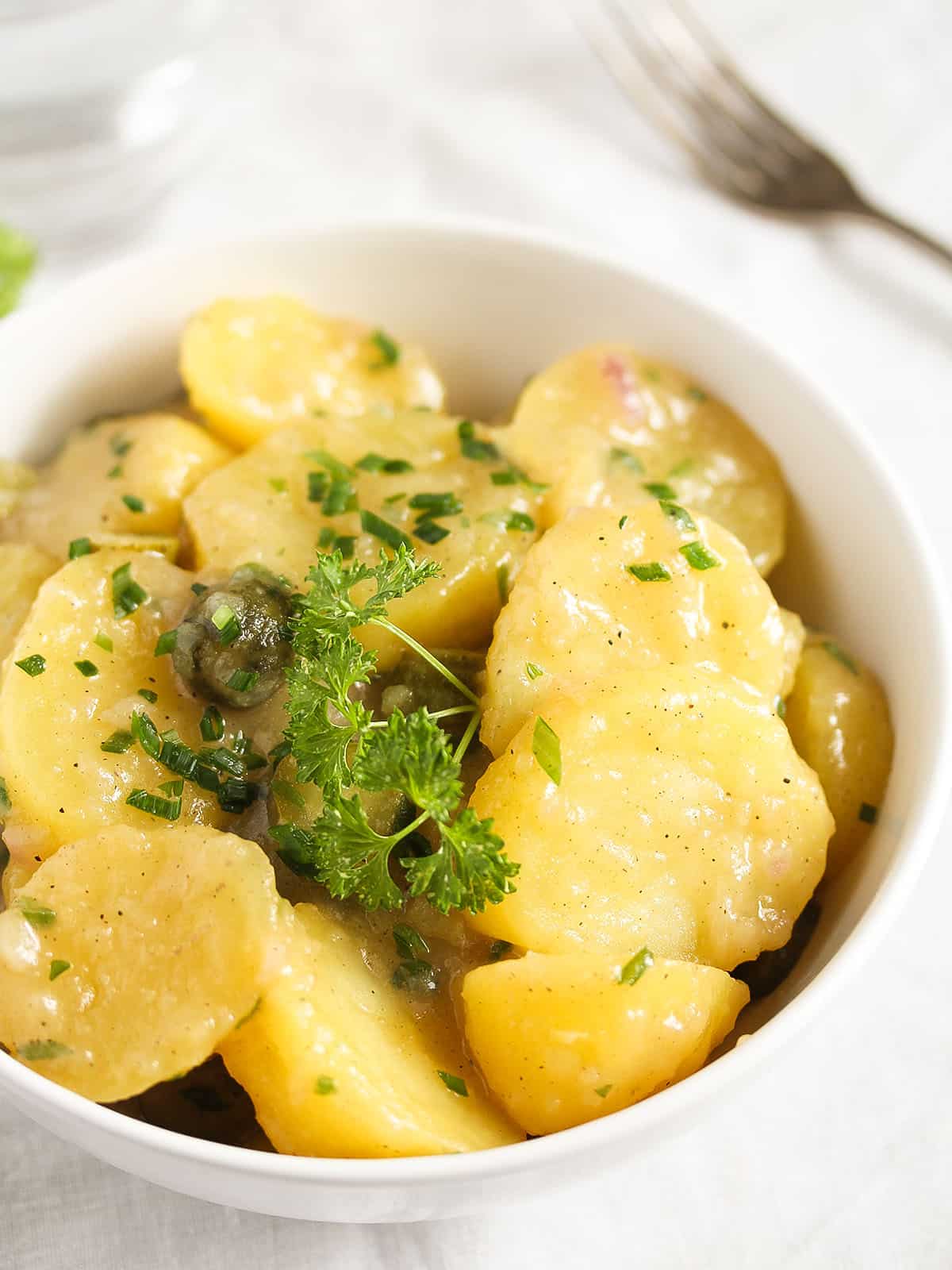 german potato salad sprinkled with chives in a white bowl.