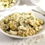 a plate full of chicken israeli couscous with zucchini and sprinkled with lots of parmesan.