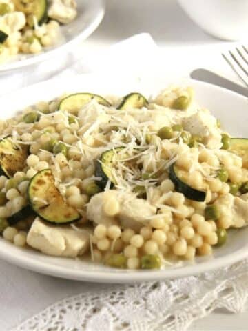 a plate full of chicken israeli couscous with zucchini and sprinkled with lots of parmesan.